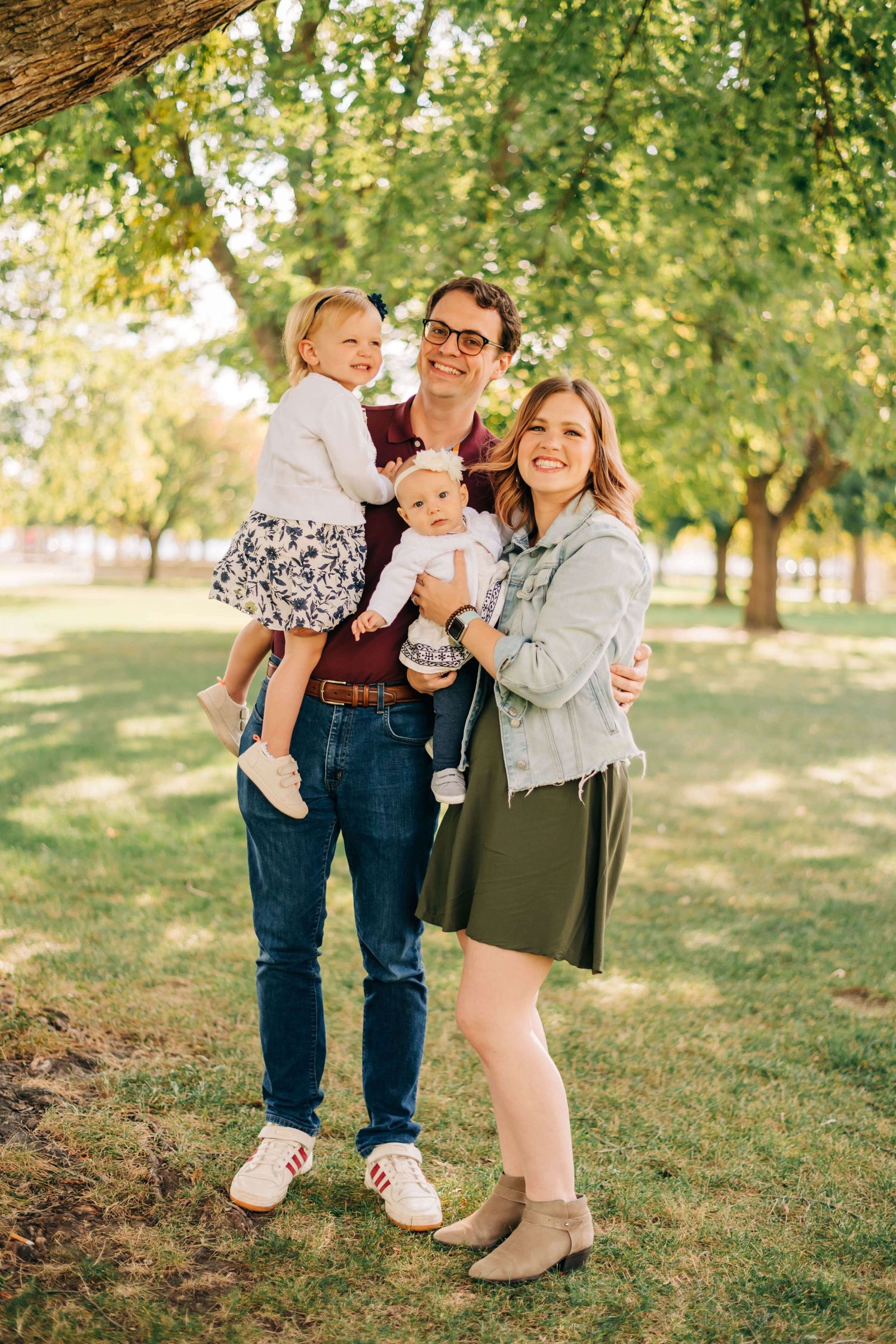 mother, father, and two little girls posing for a photo at a park
