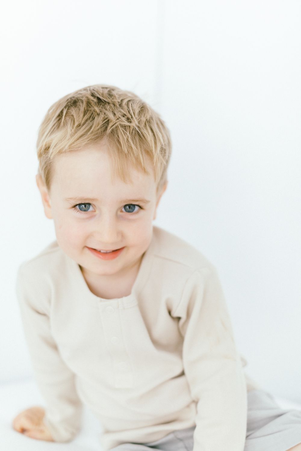 Small child in cream sweater smiling sweetly against white background.