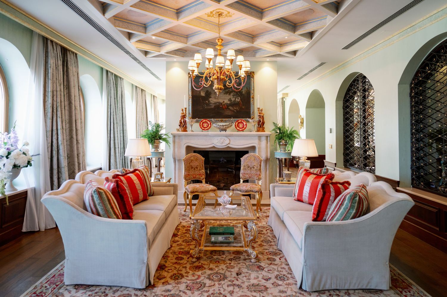 Elegant living room with white sofas, red pillows, and ornate fireplace in Spanish colonial style.