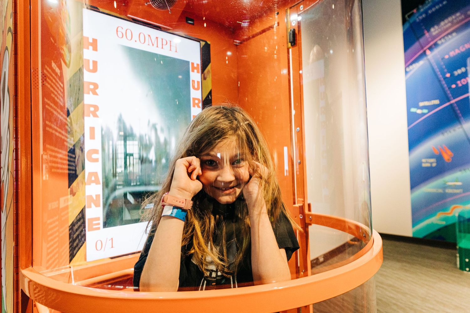 girl standing in hurricane simulator holding her ears at Monroe Science Center