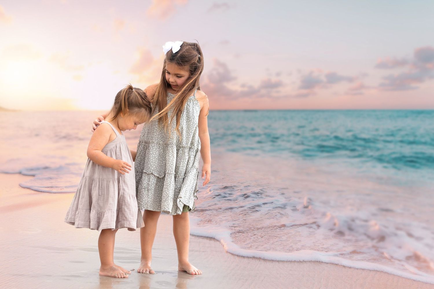 Two figures in matching dresses explore the beach shoreline at sunset.