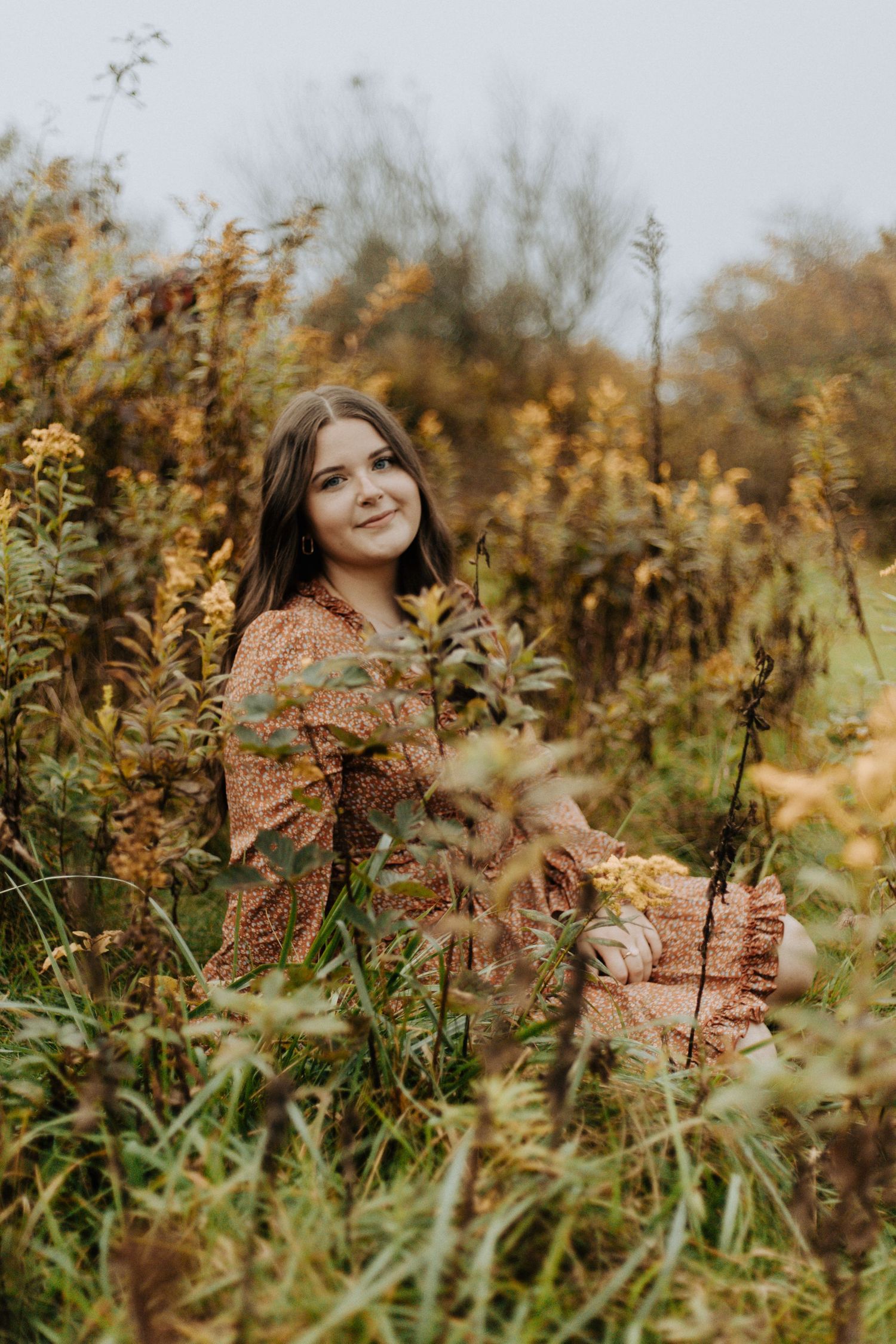 Person in floral dress sits among tall wildflowers during autumn season.