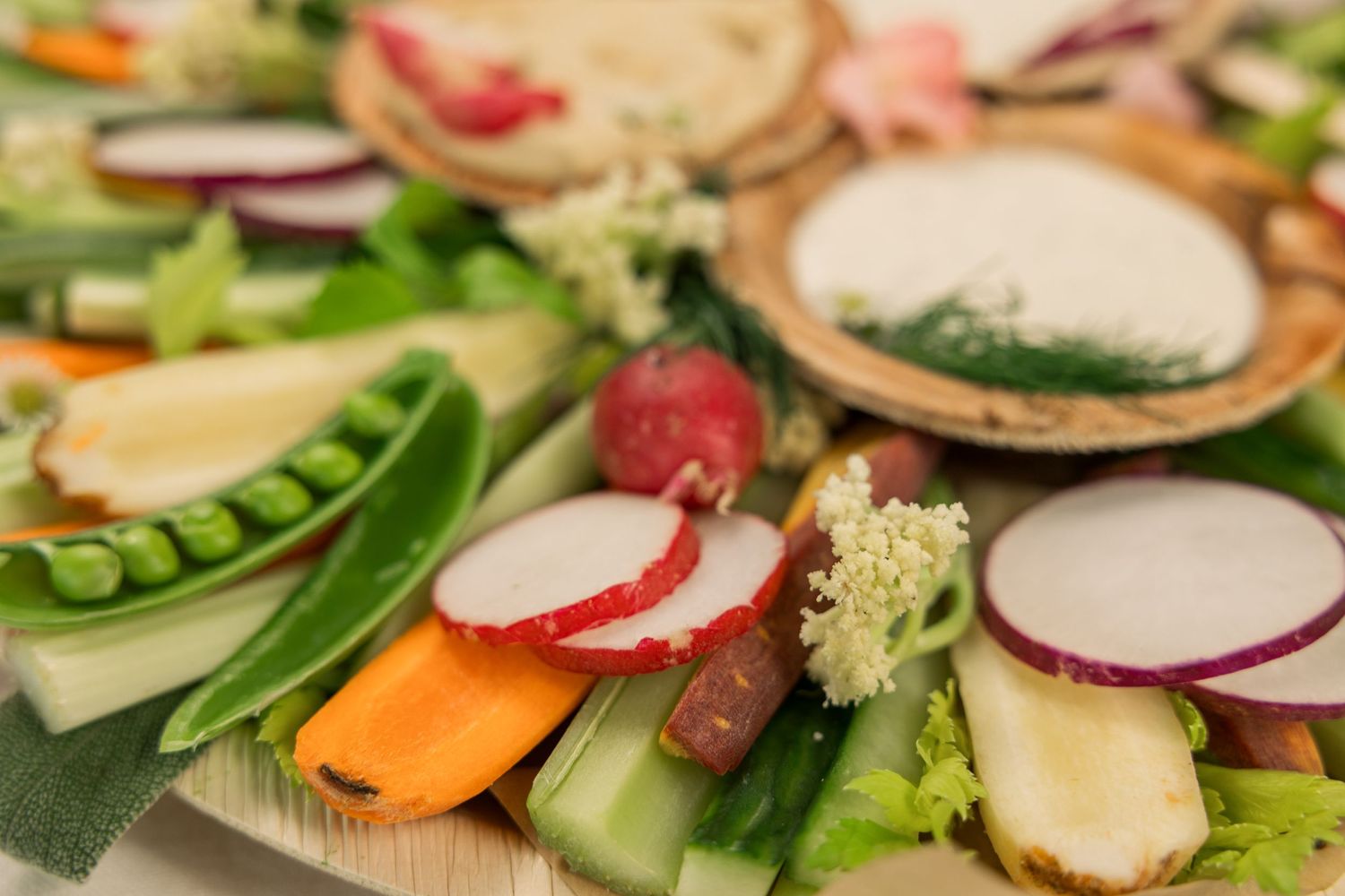 Fresh vegetable crudité platter with radishes, carrots, and dip bowls arranged artistically.