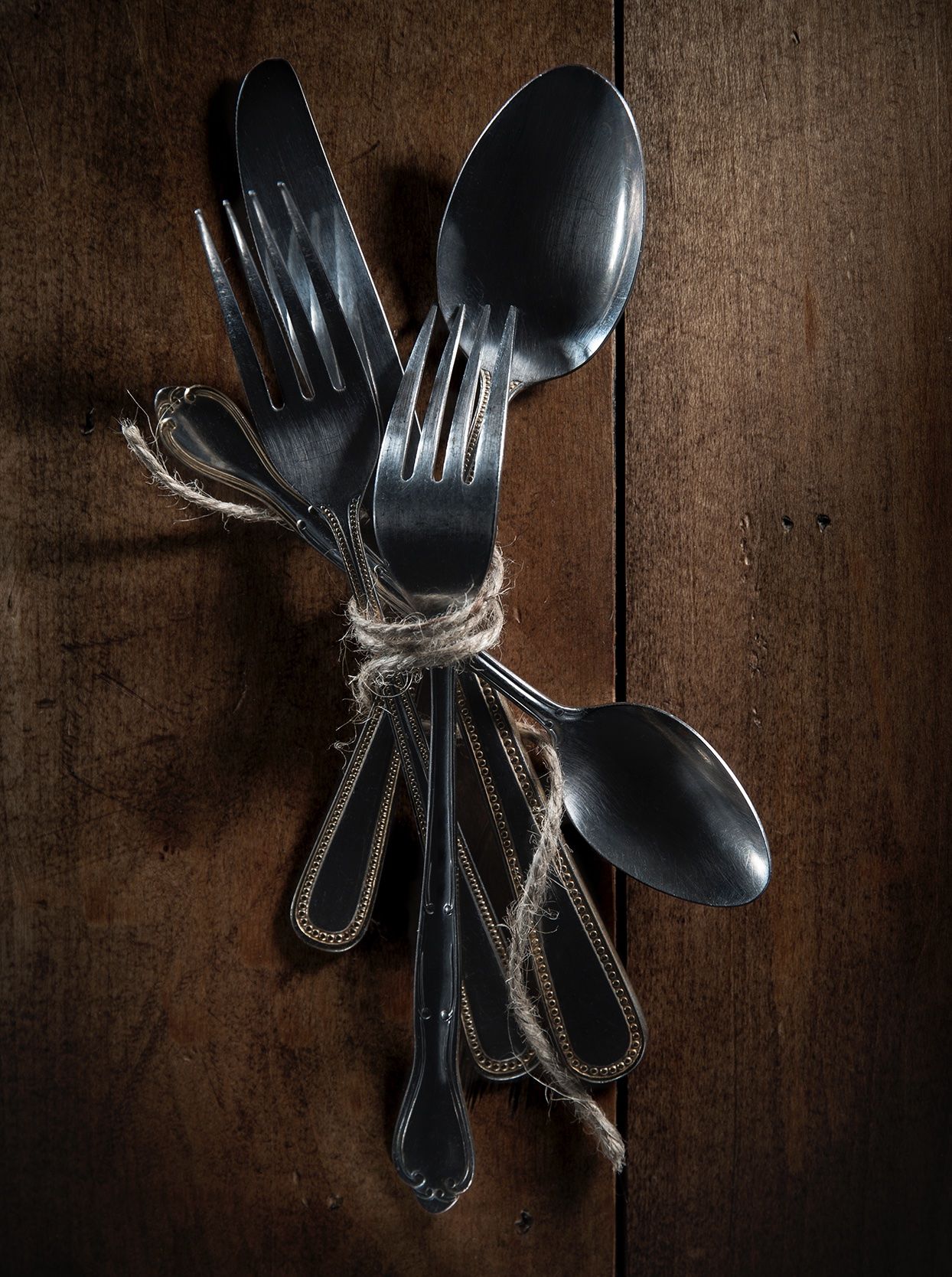 Black vintage silverware tied with rustic twine on dark wooden background.