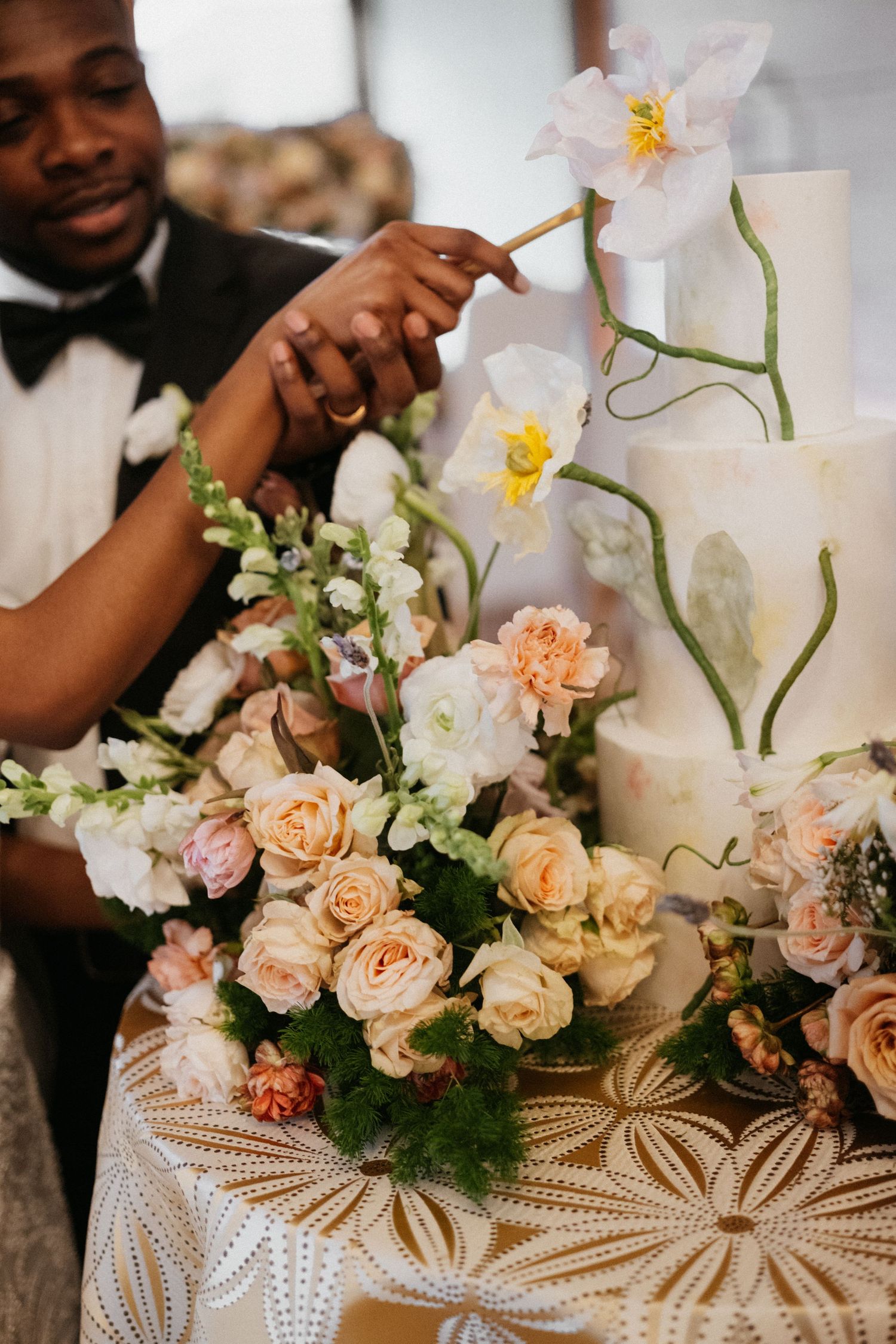 Beautiful wedding cake display with delicate orchids and peach roses on a patterned tablecloth.