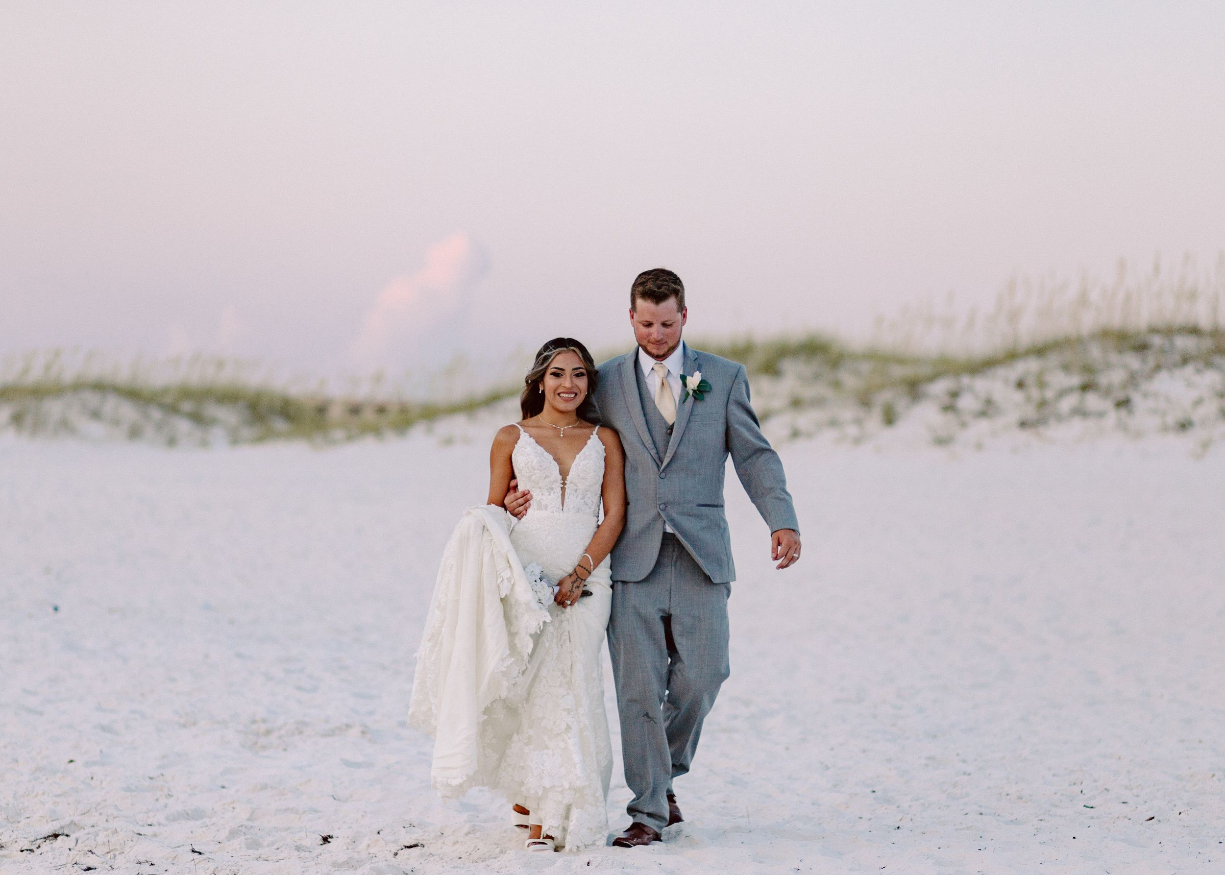Bride and groom walking together on pristine white sand dunes at dusk.