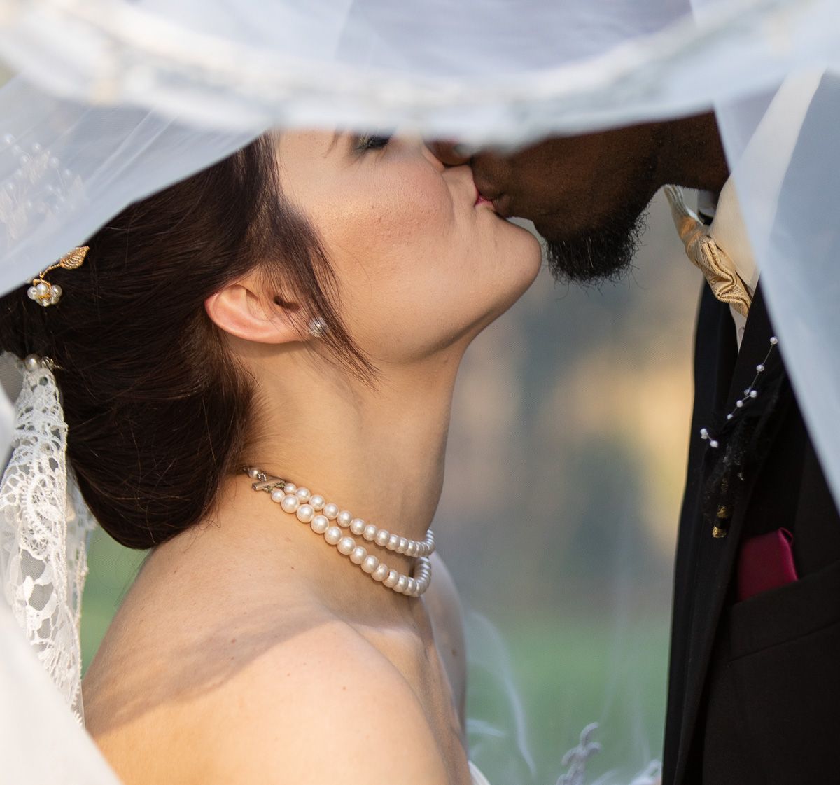 Close-up of a bride wearing pearl necklace and veil during an intimate wedding moment.