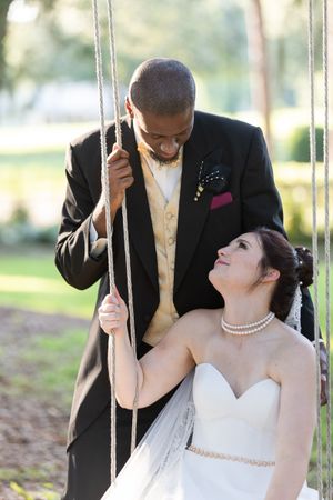 A romantic wedding photo of a couple sharing a tender moment on a swing in an outdoor garden setting.