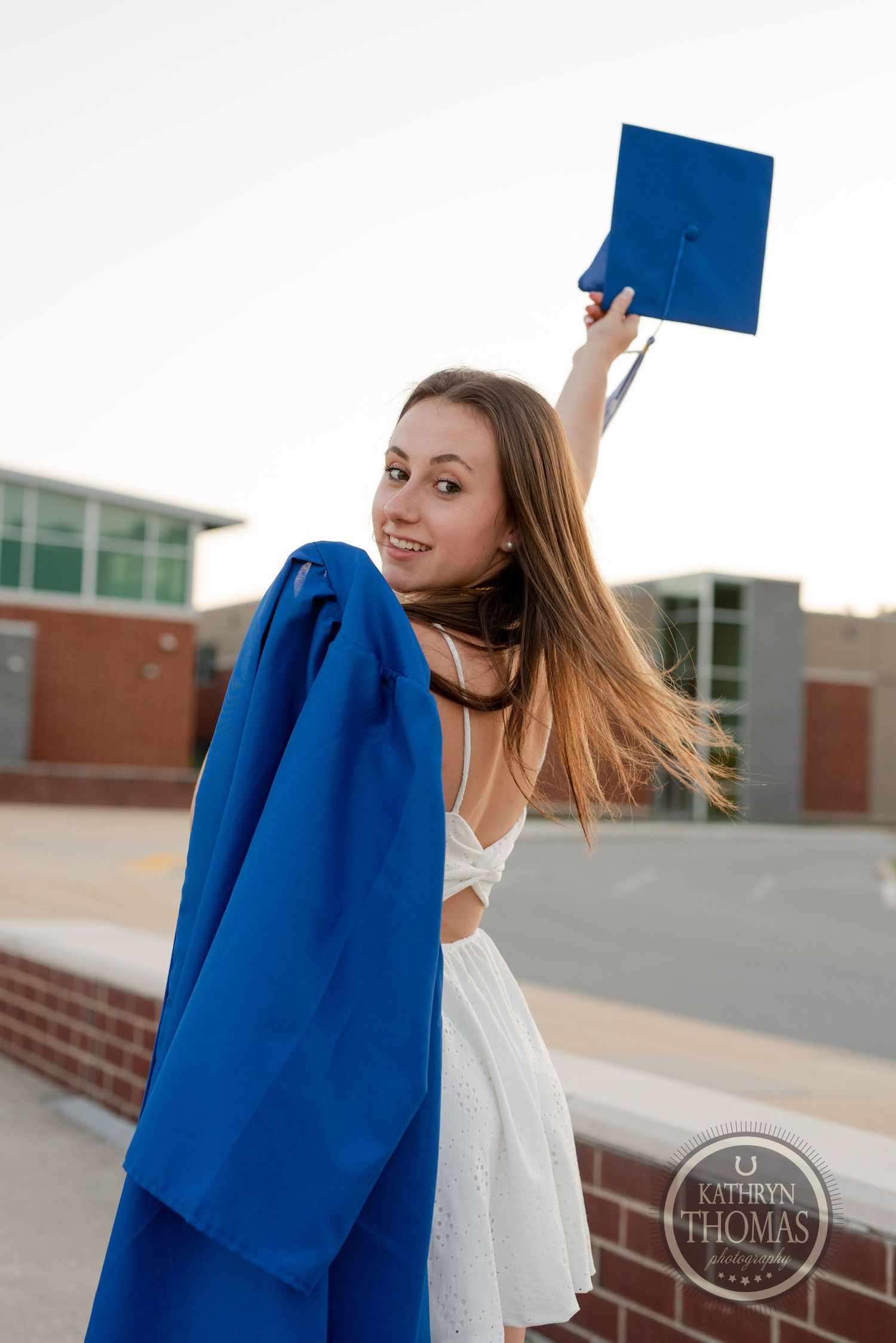 Graduate celebrating with blue cap raised high outside brick building.