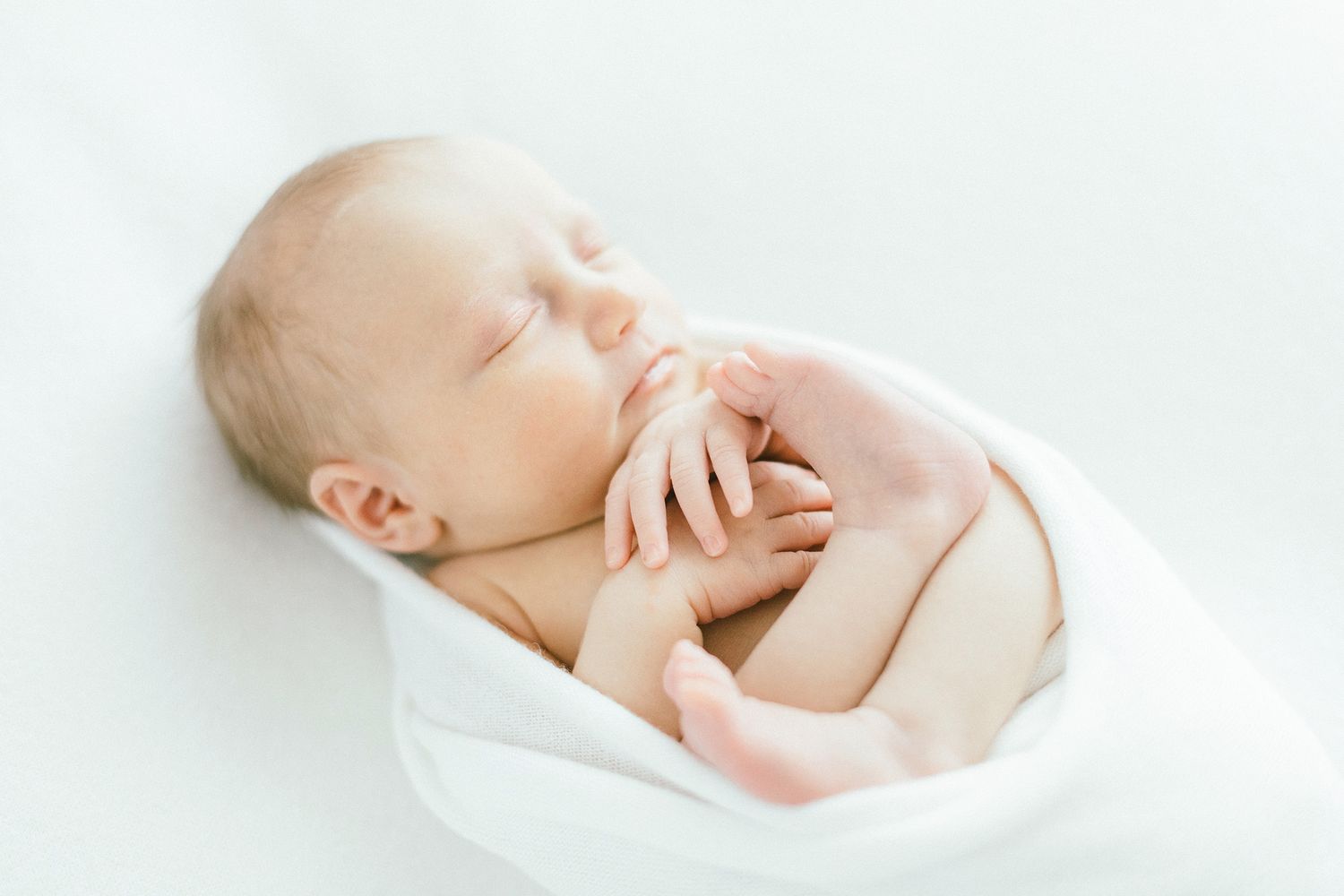 Newborn baby sleeping peacefully while swaddled in soft white blanket.