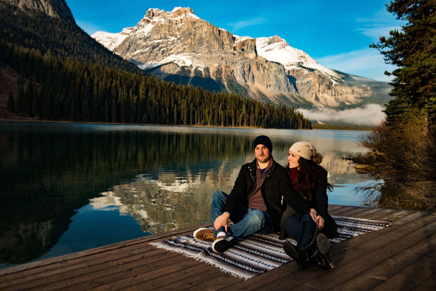 Lana and Adam engagement photo by Emerald Lake. Mountains in the distance.