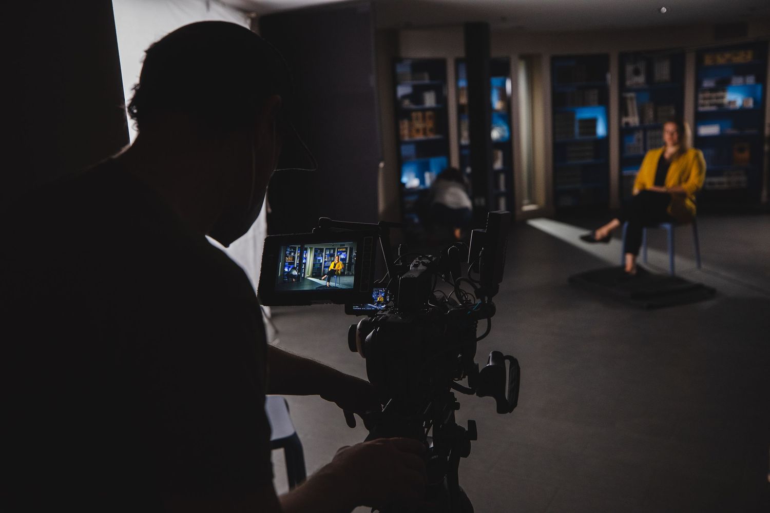Silhouetted camera operator filming interview setup in dark studio.