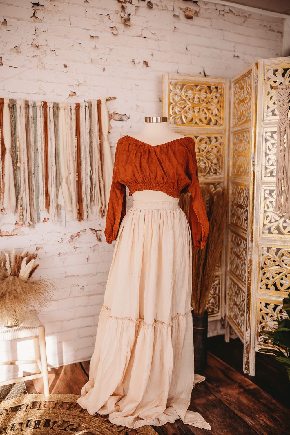 Burnt orange off-shoulder top with cream tiered maxi skirt on mannequin in boho white brick studio.