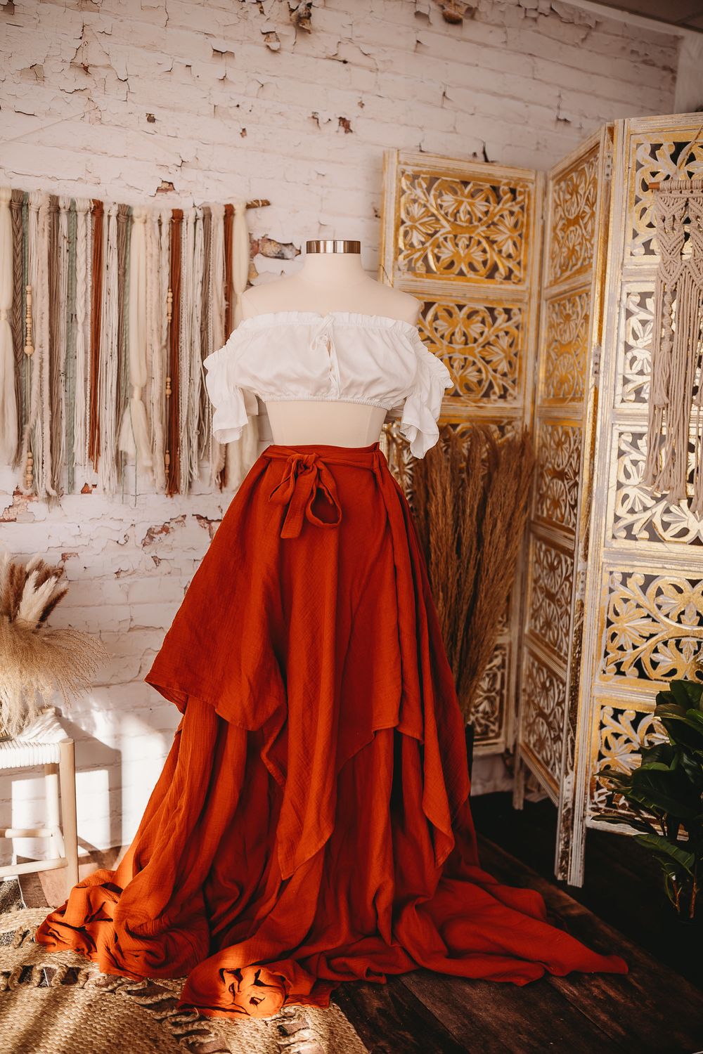 White off-shoulder crop top with rust orange high-low maxi skirt on mannequin in boho studio.