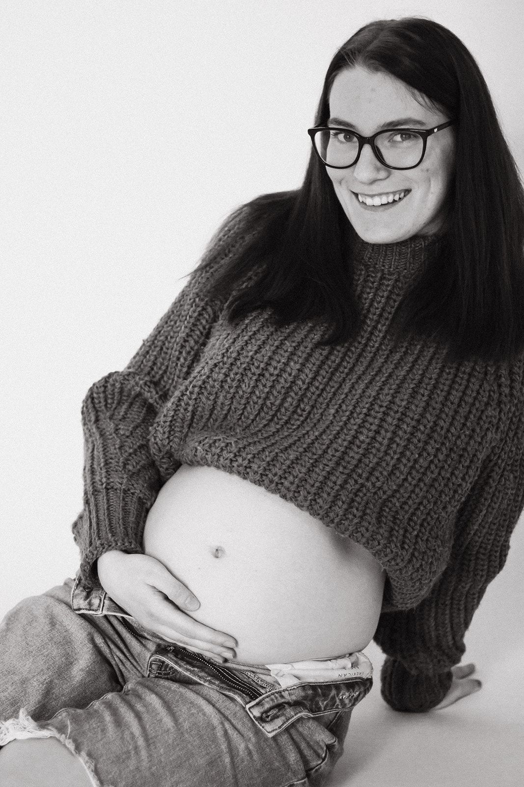 Pregnant mom holding belly in studio during maternity shoot.