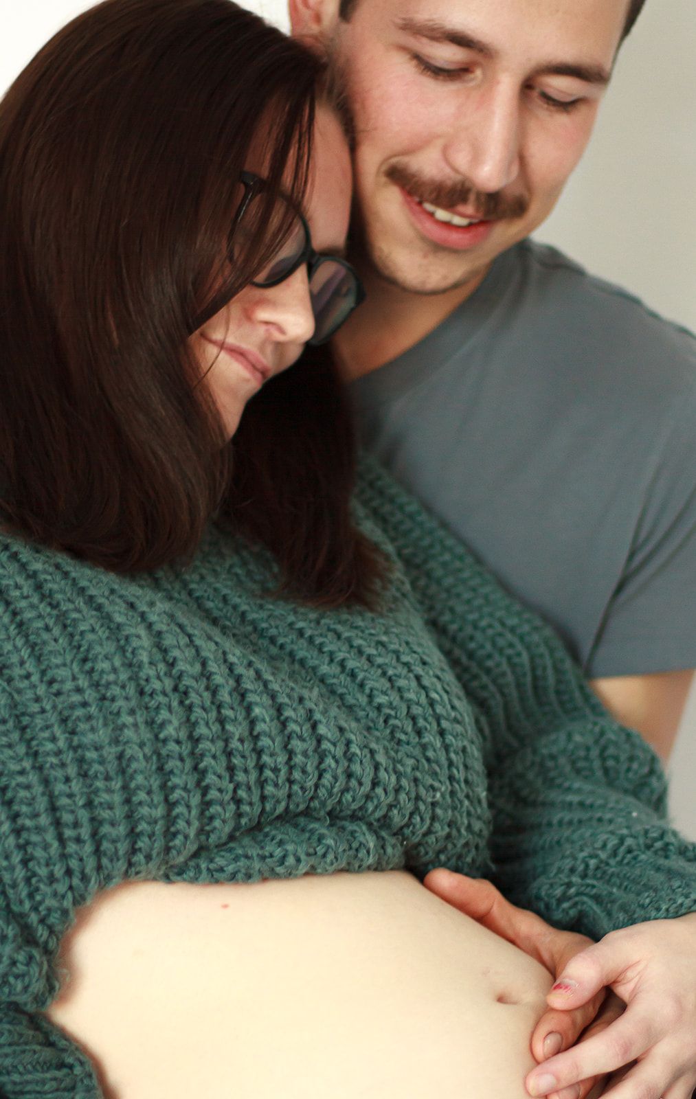 Pregnant mom and father holding belly in studio during maternity shoot.