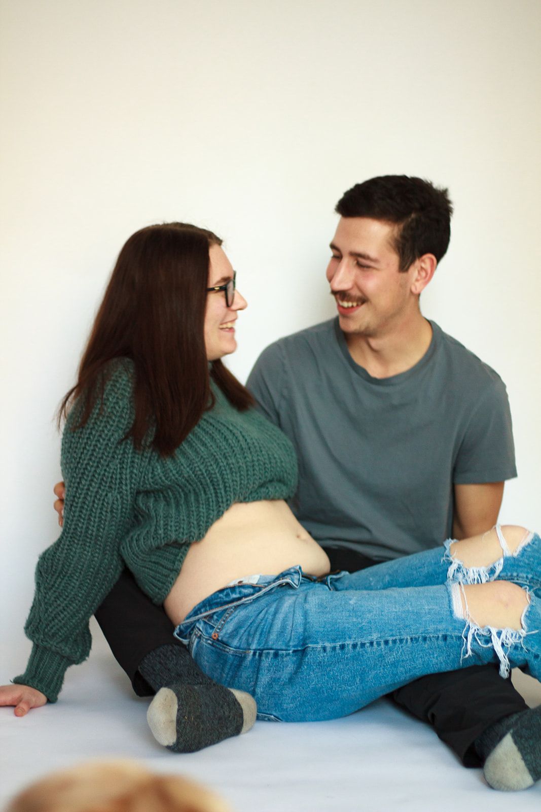 Pregnant mom and dad laughing in studio during maternity shoot.