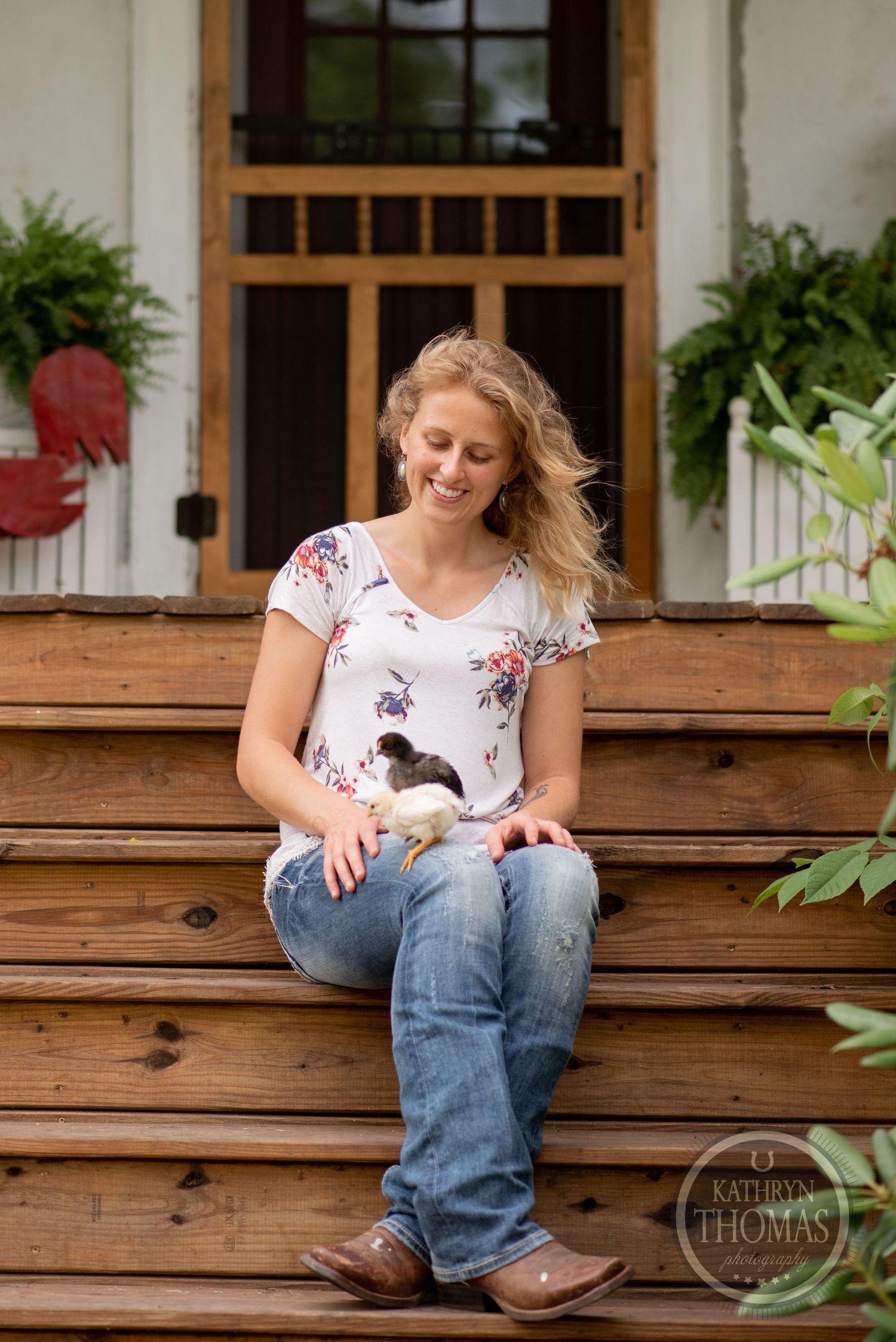 A casual outdoor portrait on wooden porch steps with hanging ferns and decorative rooster.