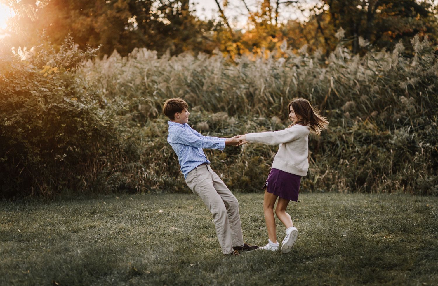 A couple spins playfully in a field during golden hour.