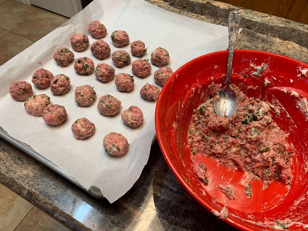 Raw meatballs arranged on parchment paper next to mixing bowl.