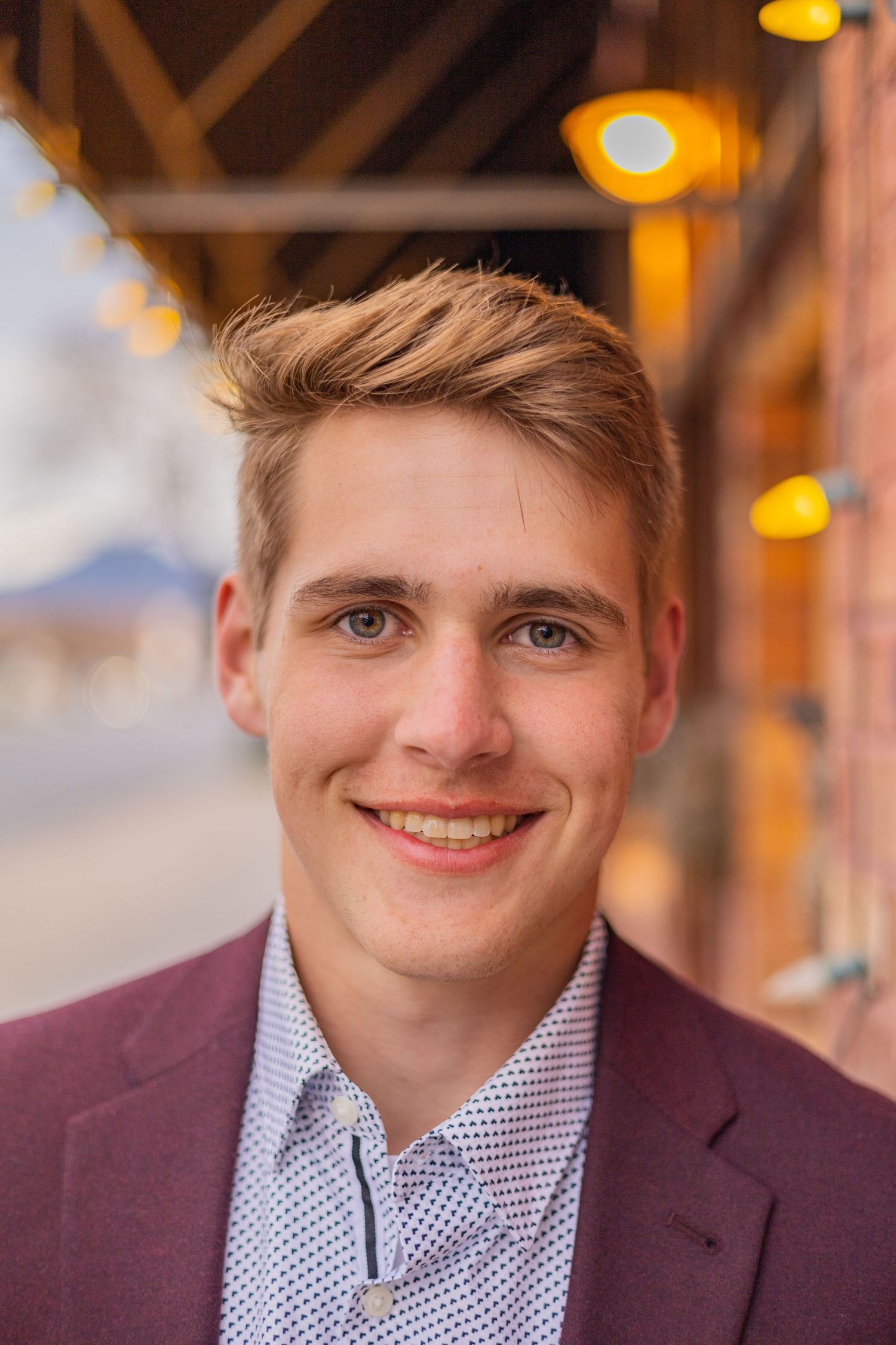 Professional headshots of someone in a burgundy blazer and patterned shirt against a warm-toned background.