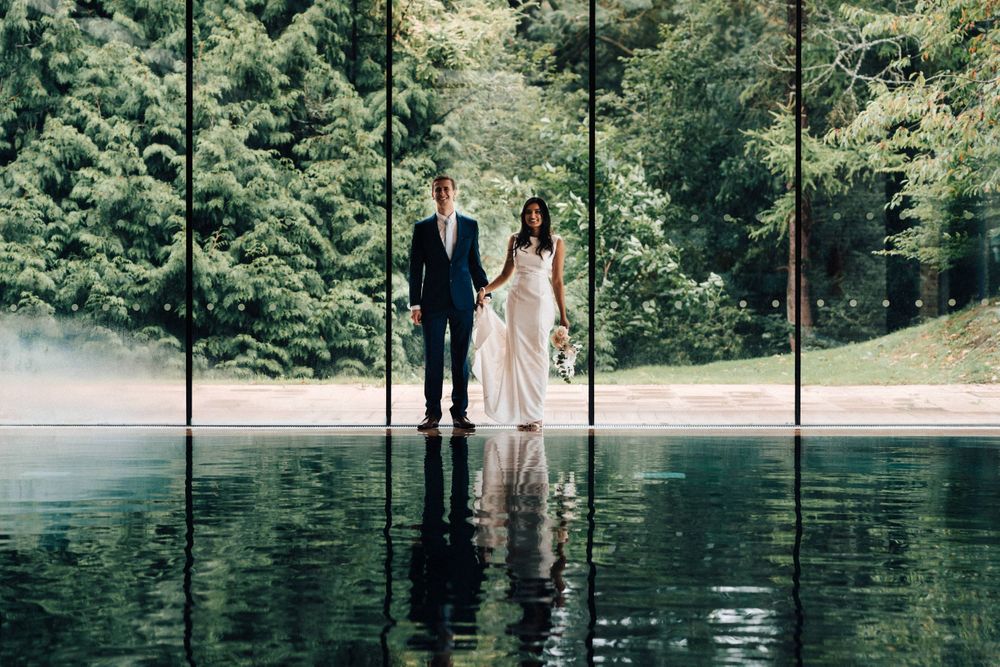 Cowley Manor classic wedding Portrait Brian Groom holding hands at the swimming pool beautiful reflection of the water