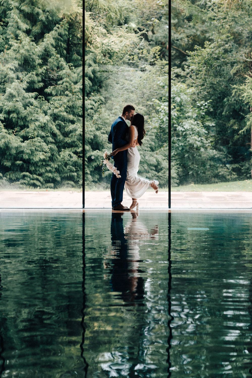 Cowley Manor wedding portrait the bride and groom are in bracing and kissing the brides leg up lovely reflections green