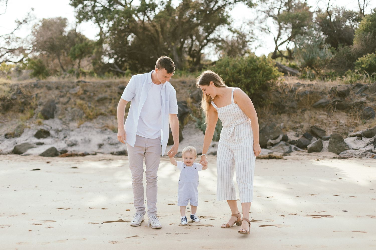 A family dressed in light colors walks together along a sandy beach at sunset.