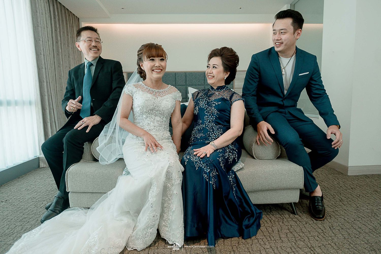 Wedding party in formal attire sitting together on a luxurious couch in a modern interior setting.