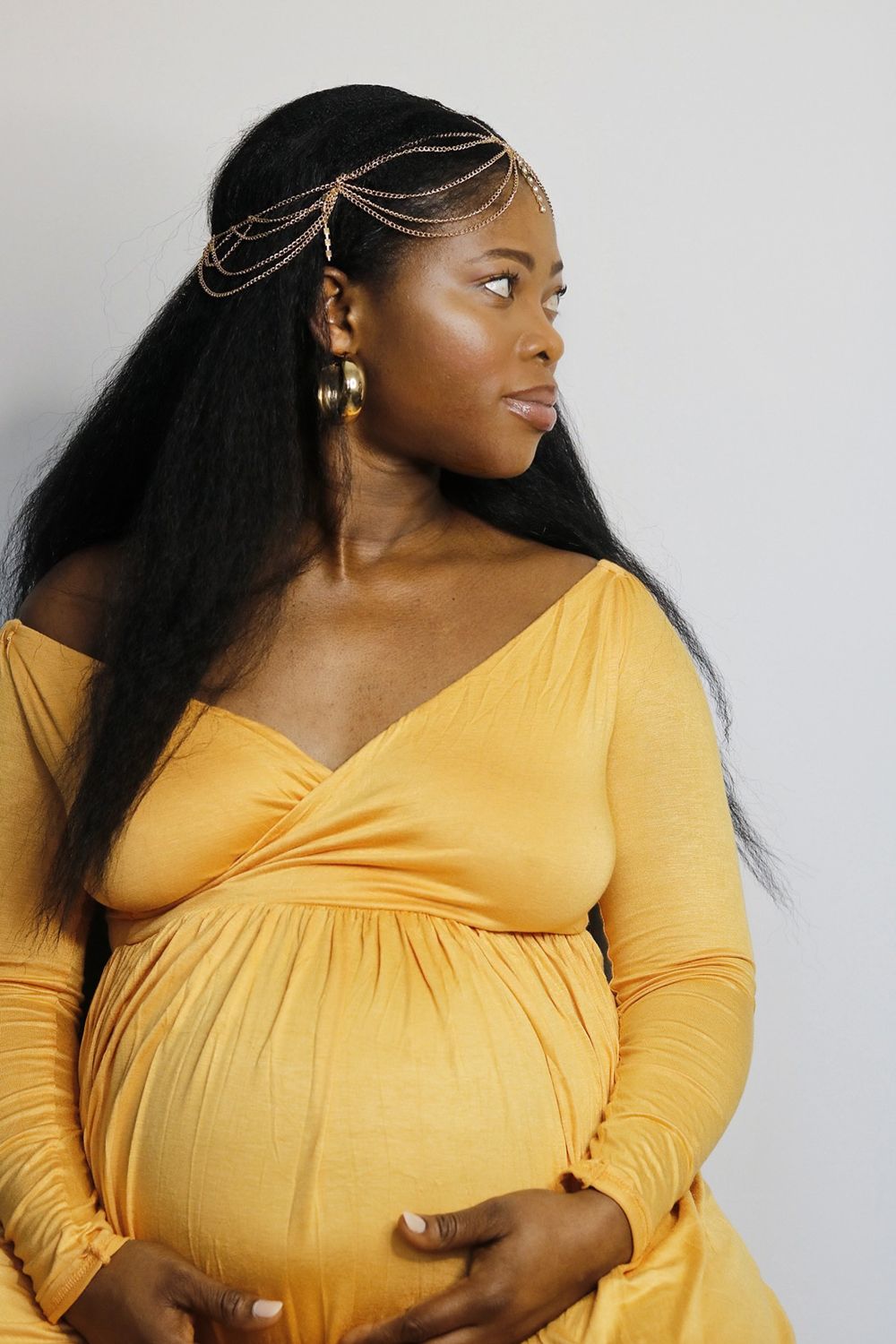 Maternity portrait featuring woman in yellow dress with ornate gold headpiece looking to the side.