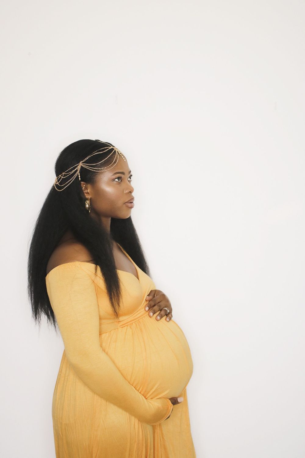 Side profile maternity portrait against white background with woman in flowing yellow dress.