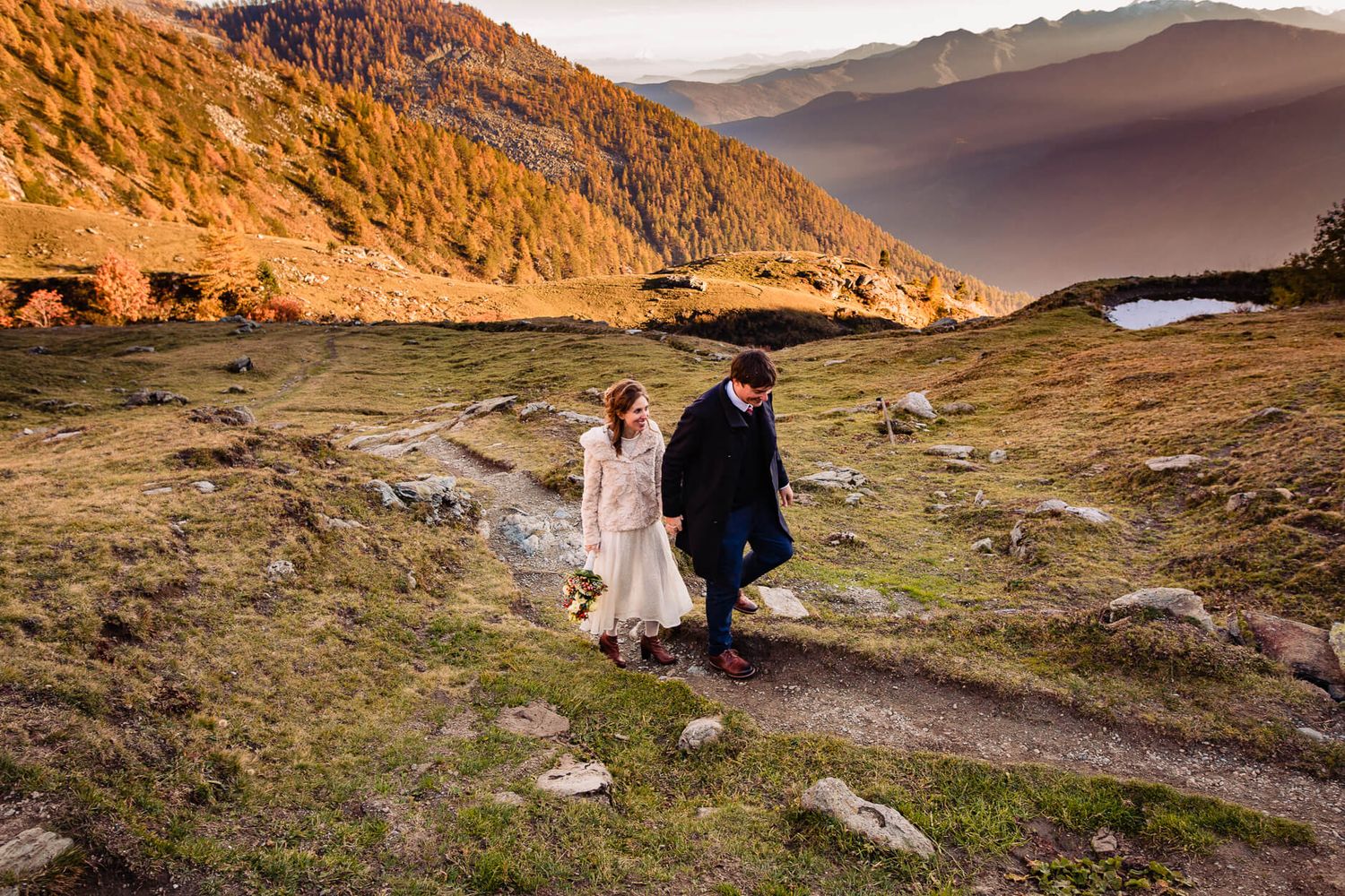 Couple walking through mountainous terrain during sunset for dramatic wedding photography.