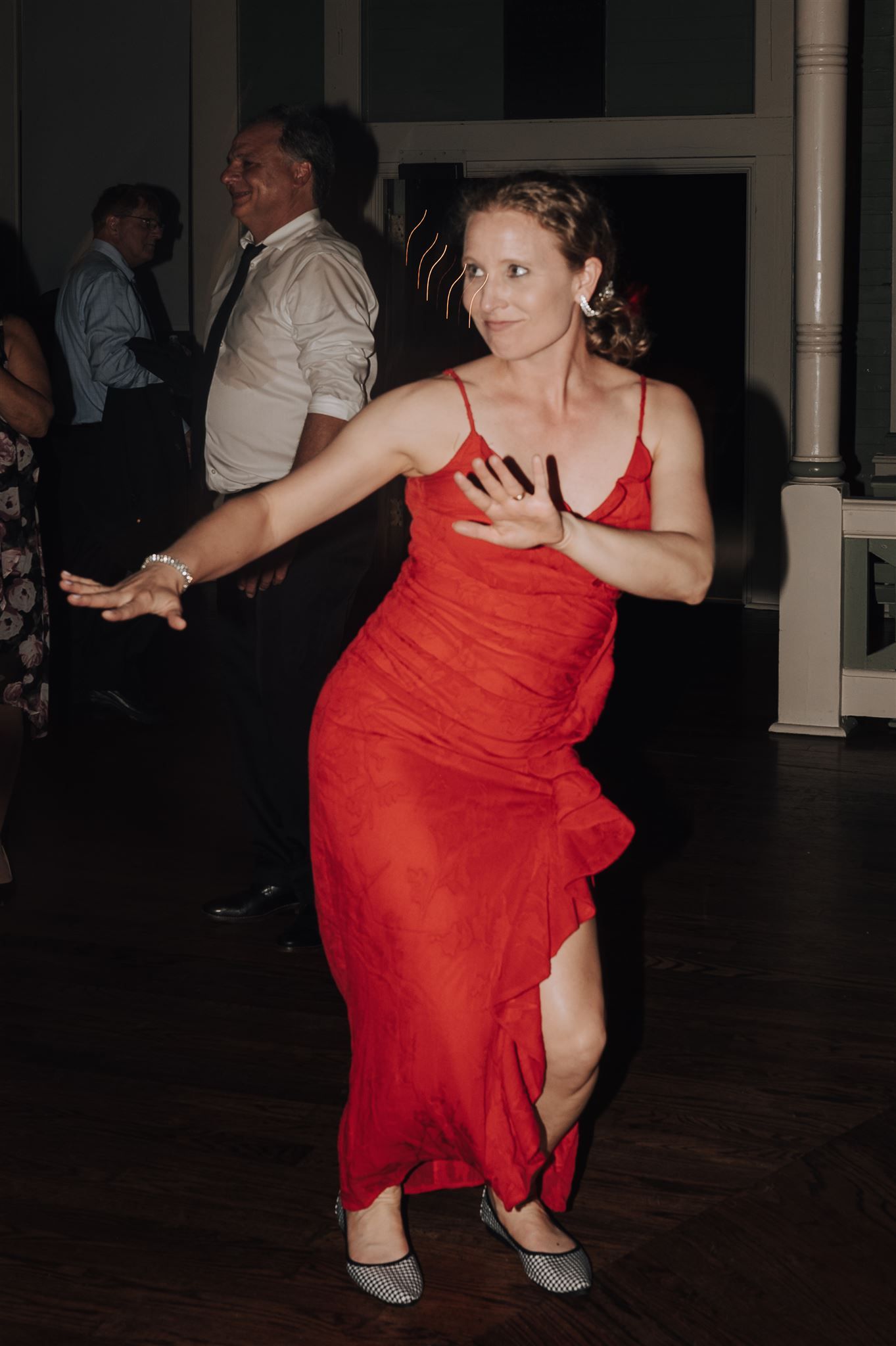 A woman in a vibrant red dress dances energetically on a wooden dance floor.