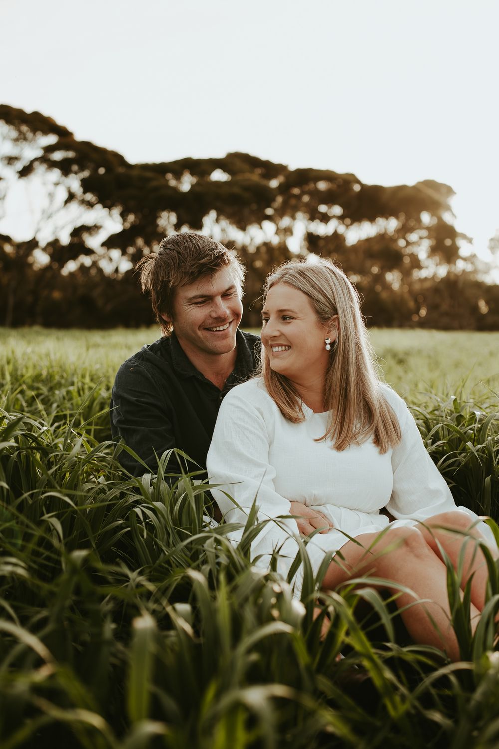 Couple sharing intimate moments while sitting in a lush green field at sunset.