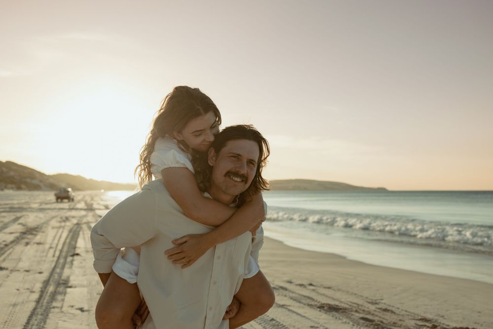 Two people embracing on a scenic beach during sunset with waves in the background.