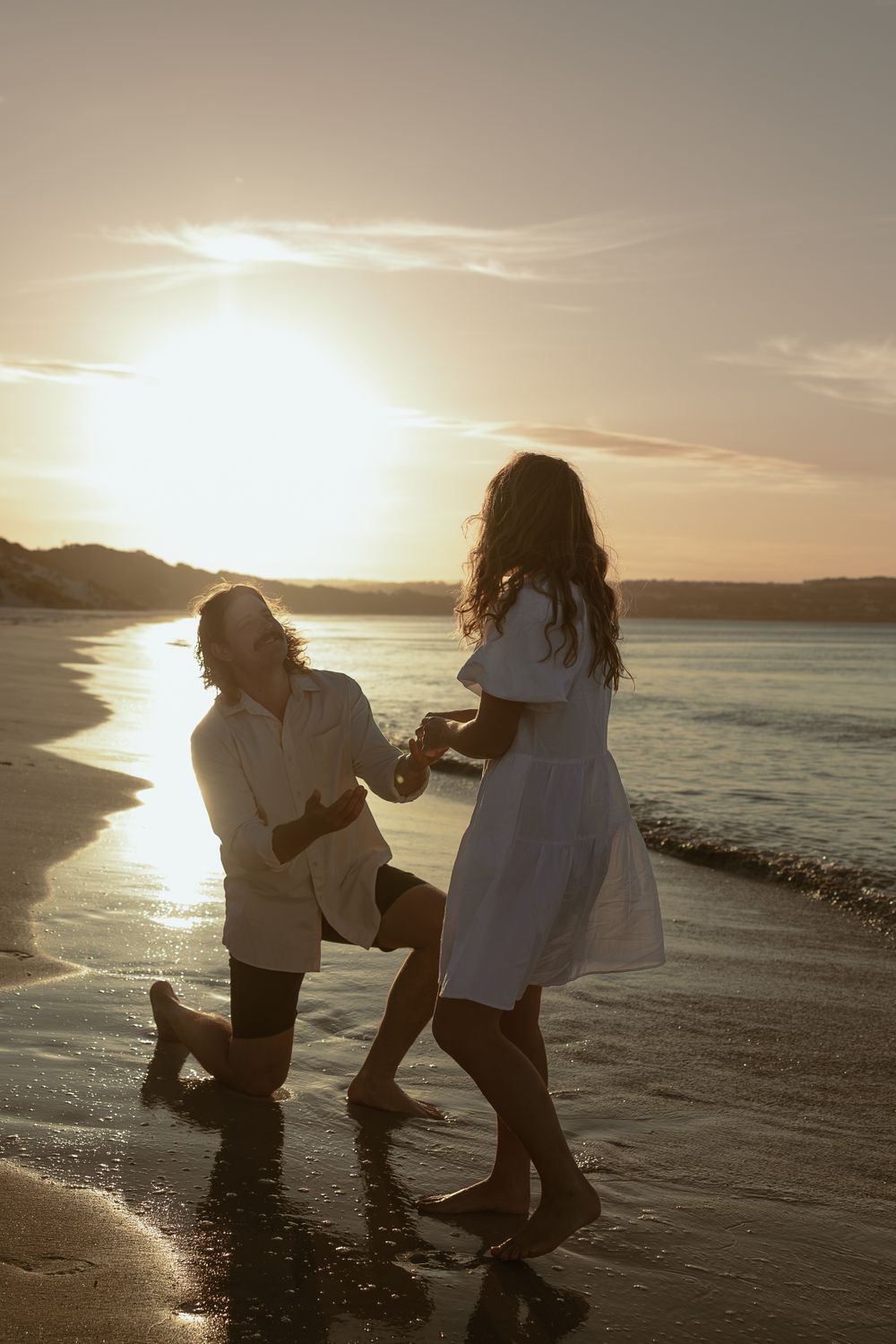 Two people playing and splashing in shallow ocean water during a golden sunset.