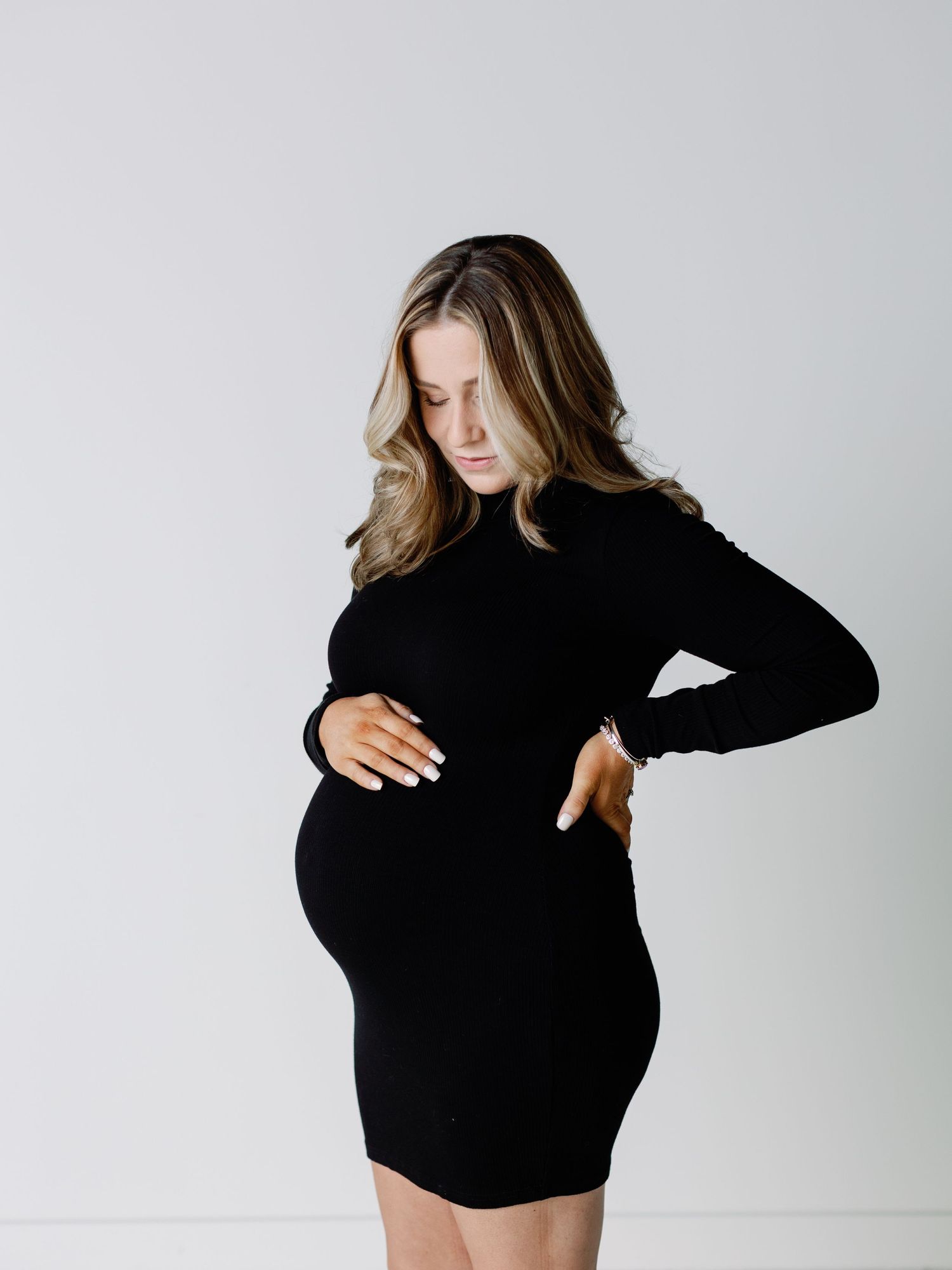 Woman in black dress showing pregnancy bump against white background.