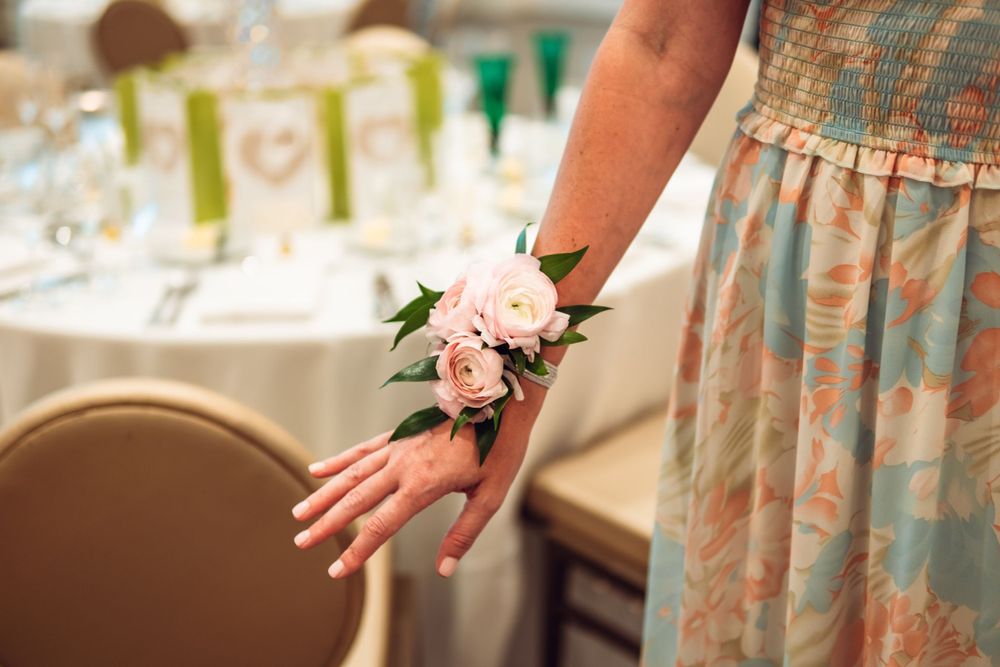 Delicate pink corsage on someone's wrist with vintage-style dress fabric in background.