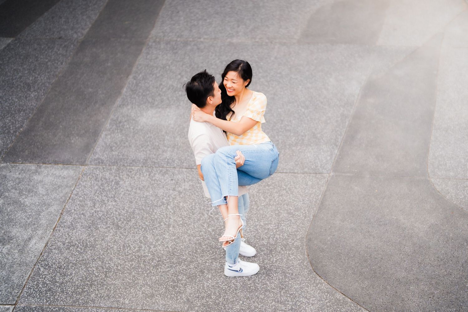 A joyful moment captured between a couple in casual wear on a gray concrete background.