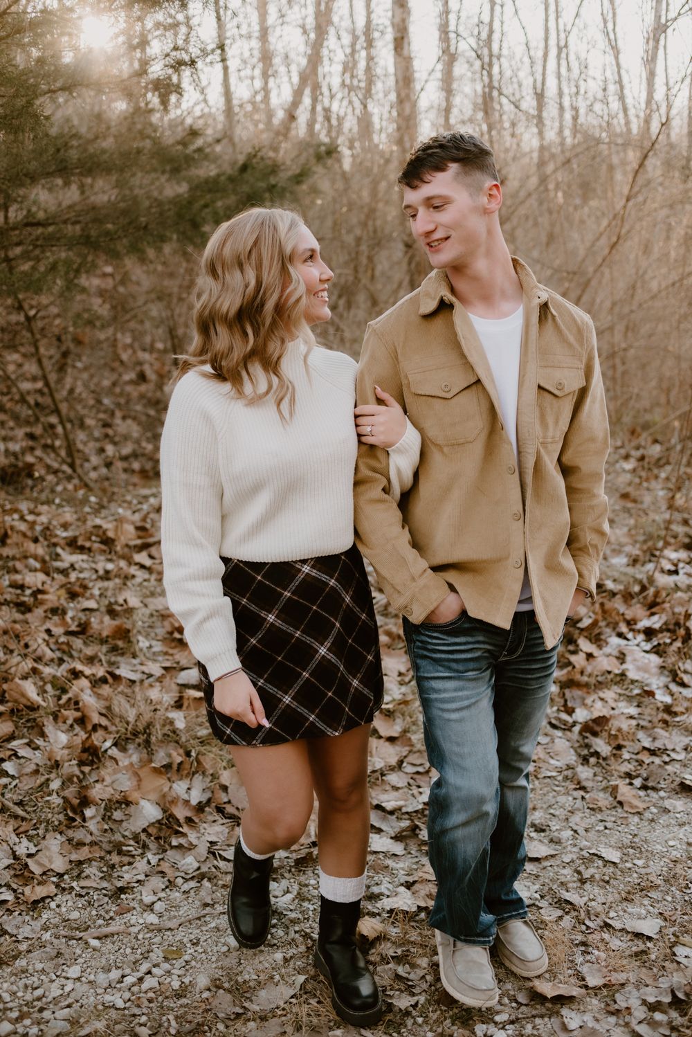 Couple walking together on leaf-covered ground wearing contrasting white and tan outfits.