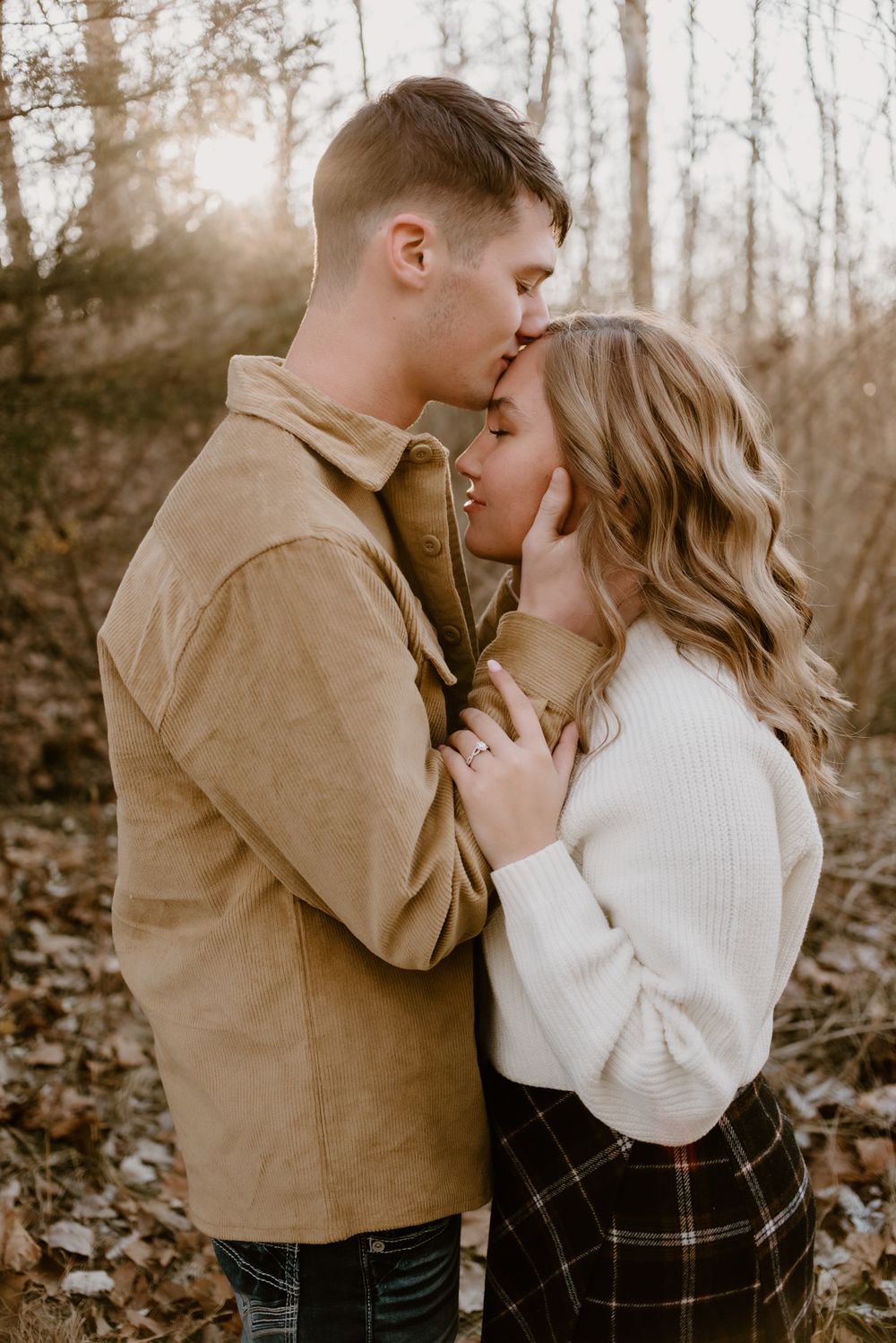 A romantic couple shares intimate moments in a wooded setting wearing casual fall attire.