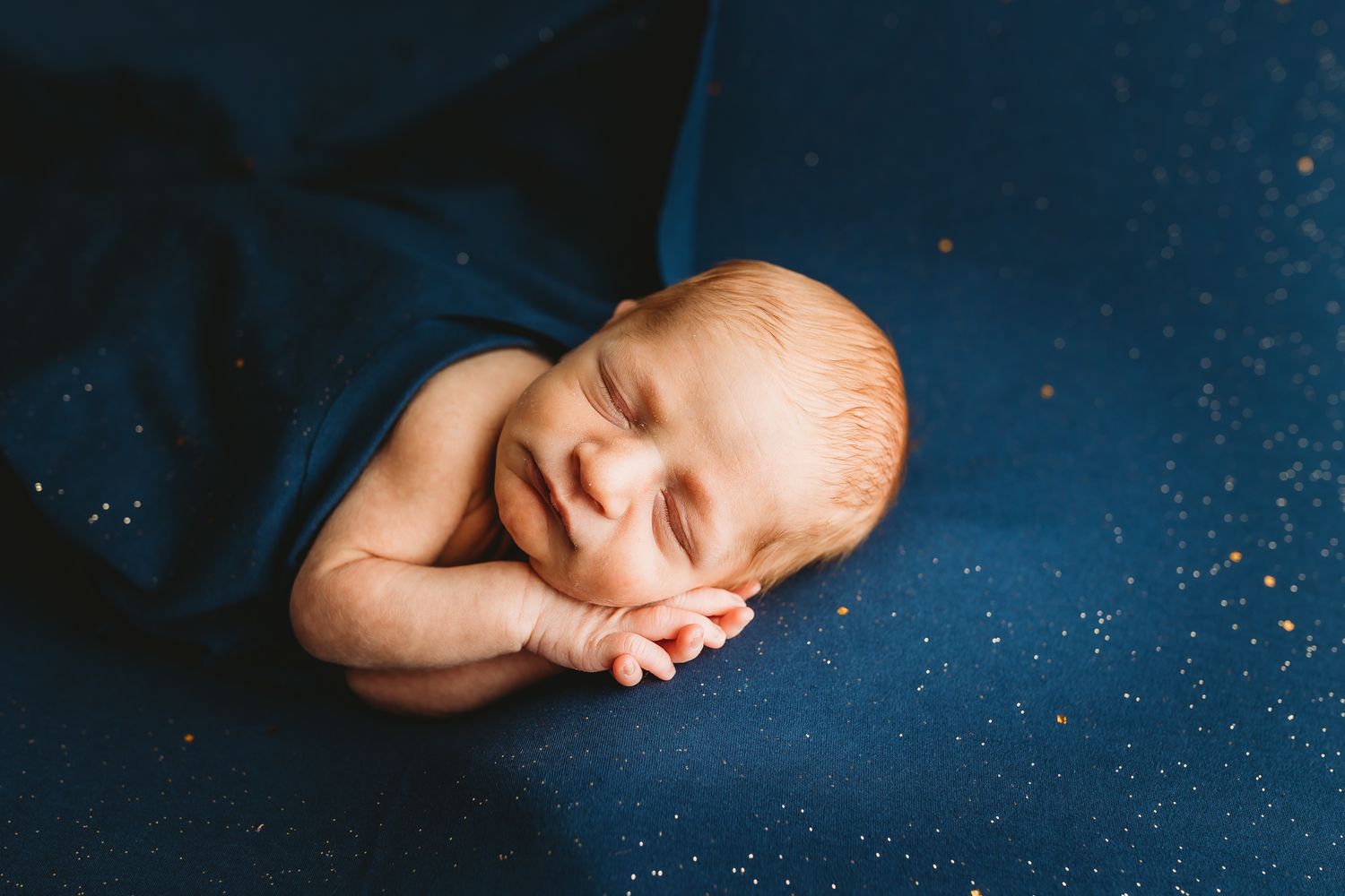 Peaceful newborn baby sleeping wrapped in navy blue blanket.