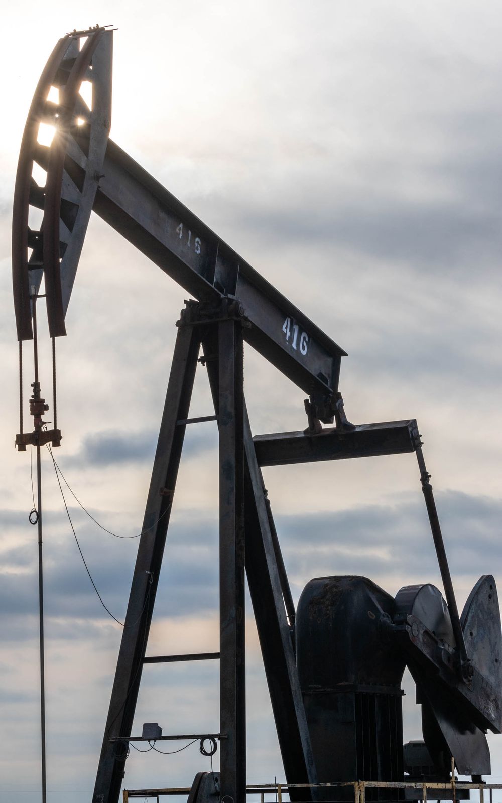 Row of oil pump jacks silhouetted against a dramatic cloudy sky.
