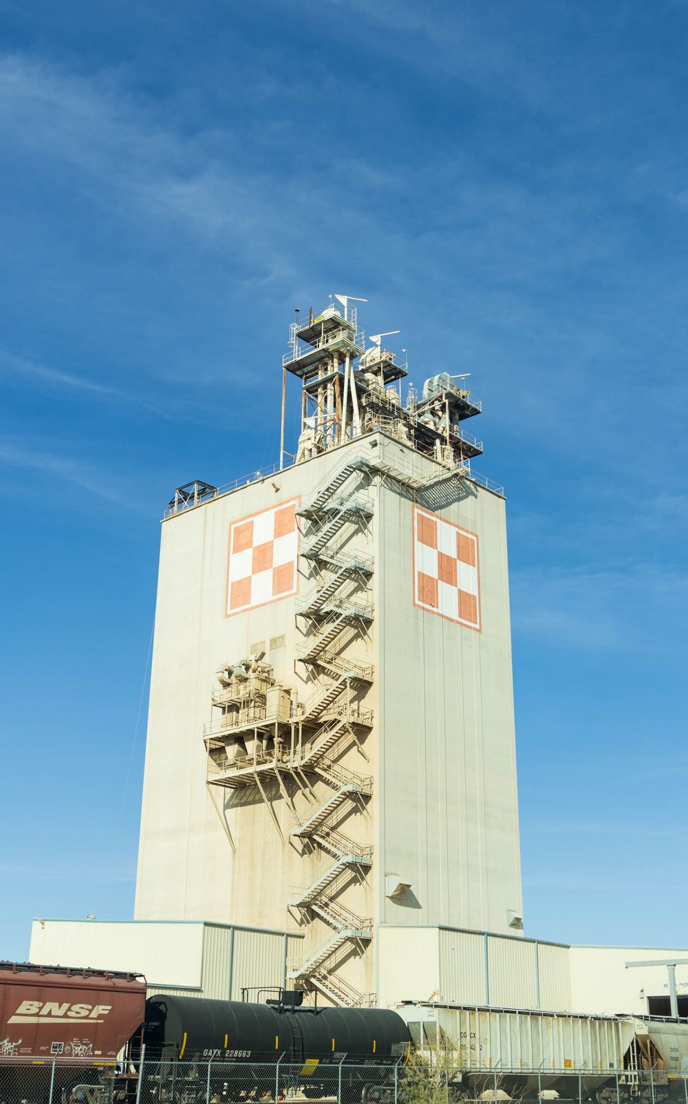 Large industrial grain elevators with red cross symbols against bright blue sky.