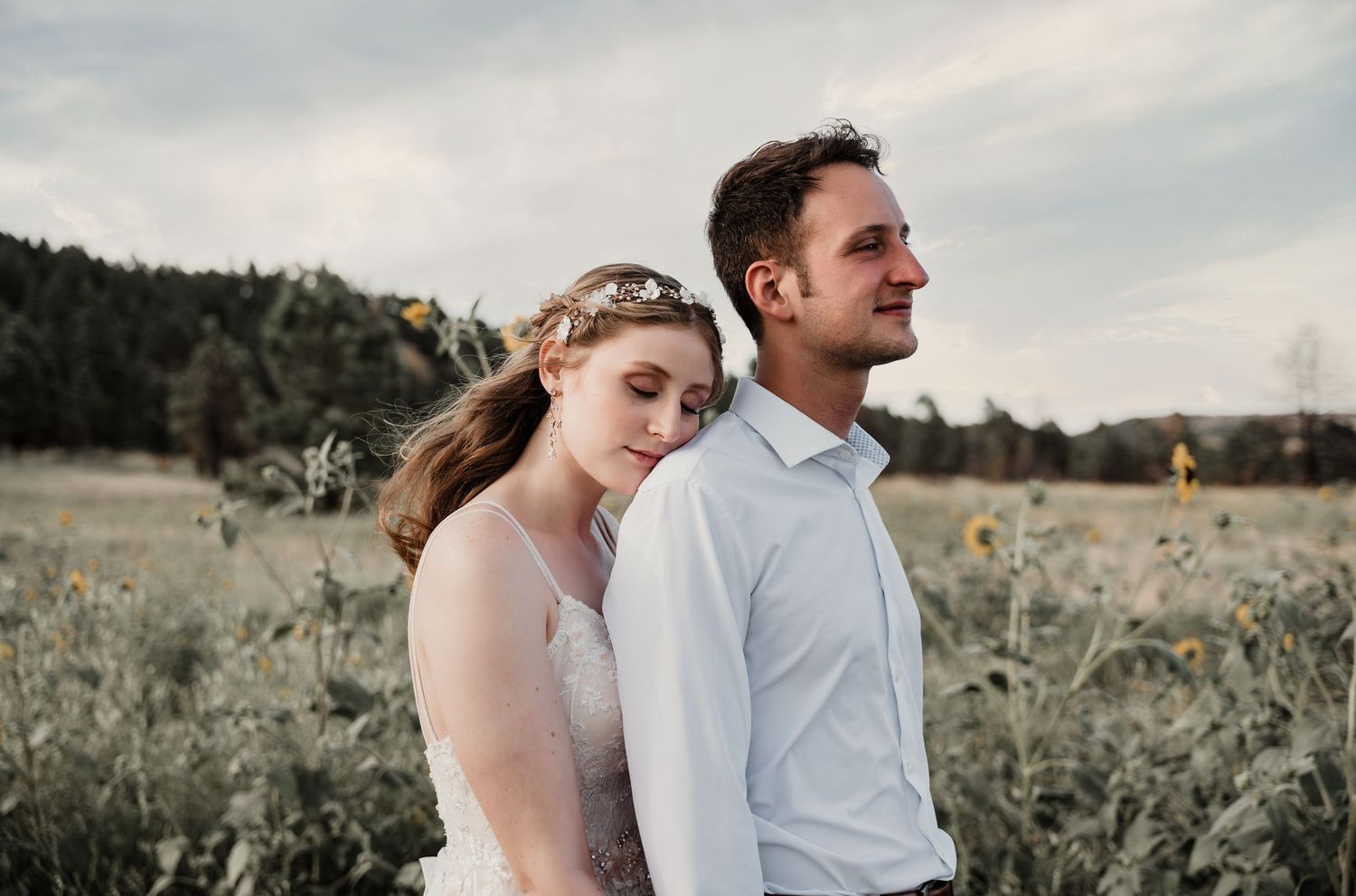 Couple embraces in field of wildflowers during golden hour sunset.