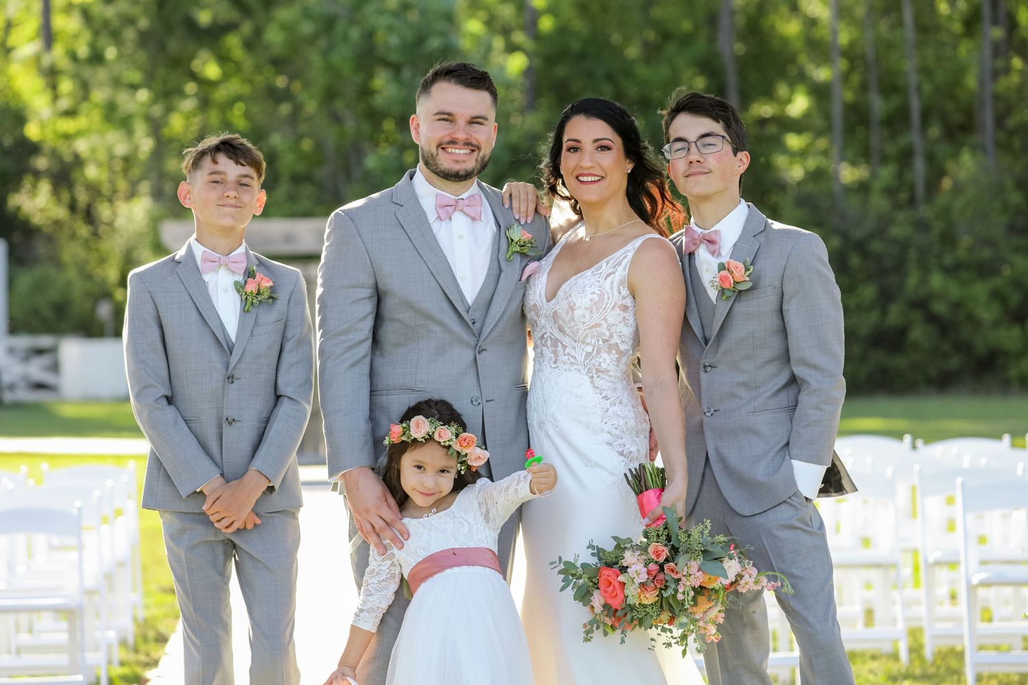 Wedding party poses together outdoors in coordinated gray attire with floral accents.