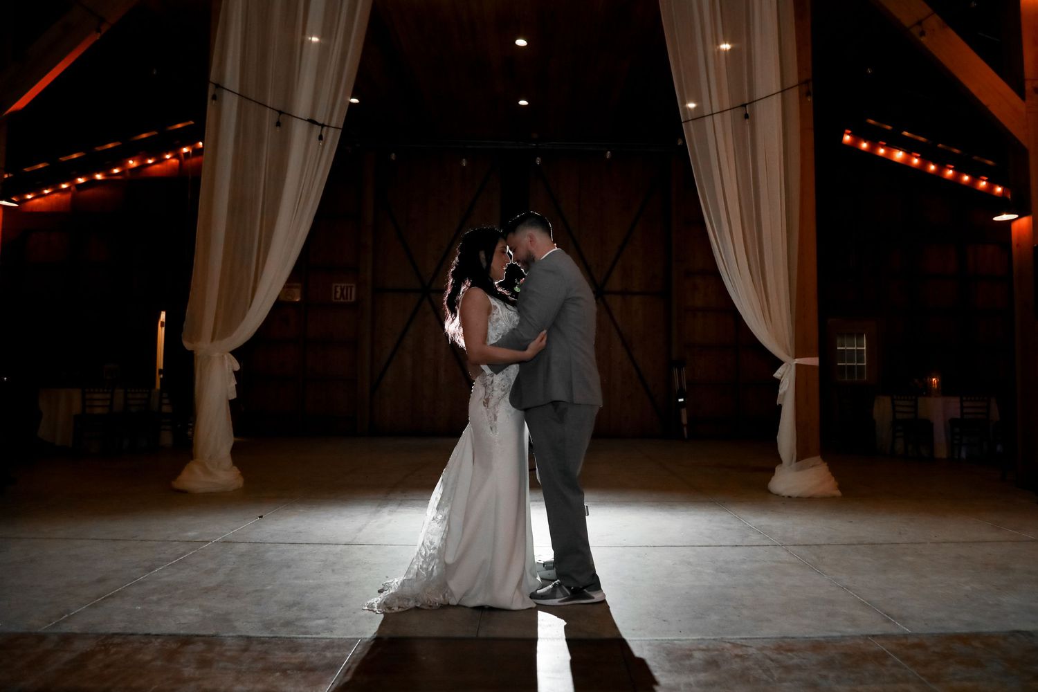 A dramatic silhouette of a couple sharing their first dance in a beautifully lit barn venue.