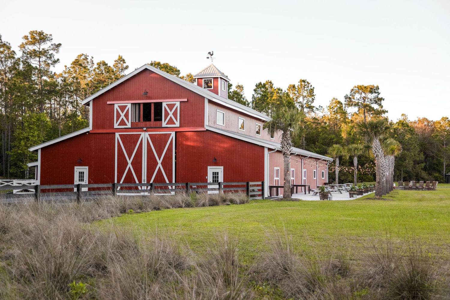 A classic red barn with white trim stands in a grassy field during golden hour.