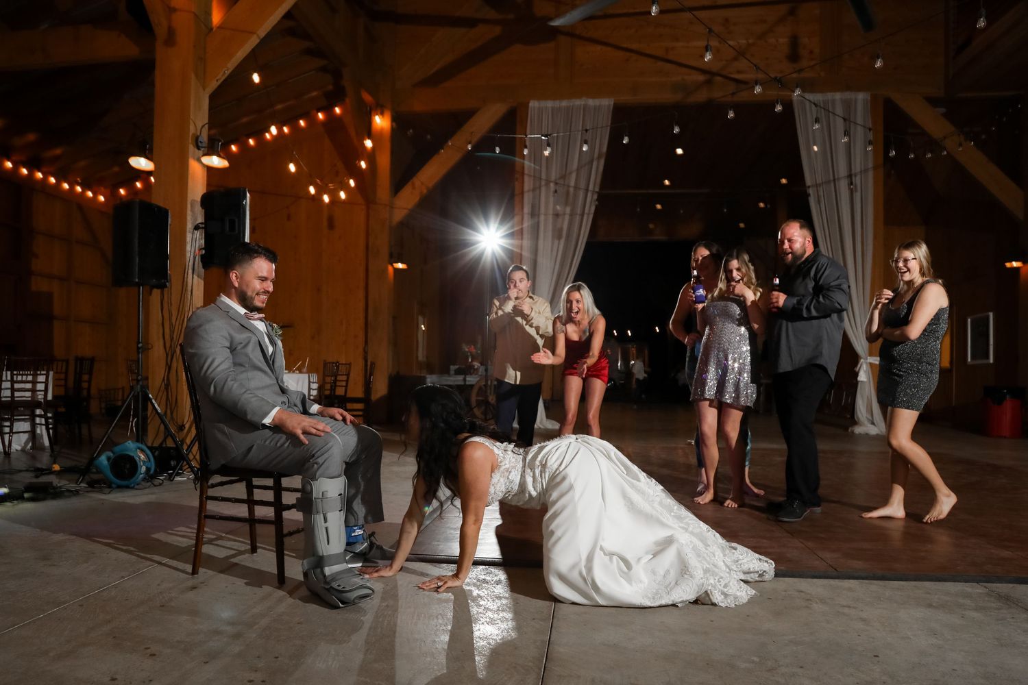 A wedding reception scene in a rustic barn venue with string lights and flowing curtains.