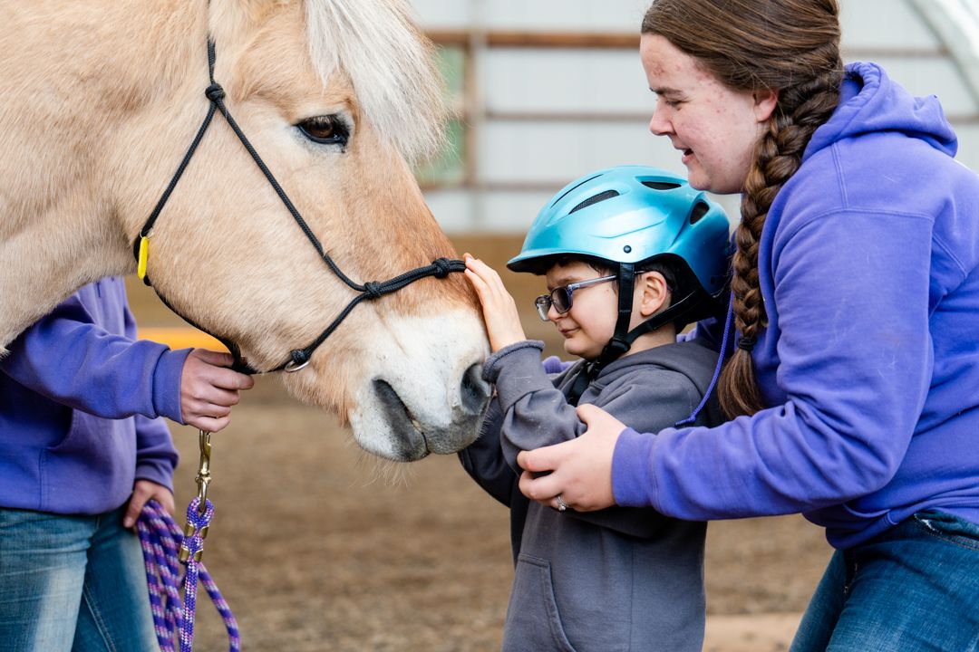 staff helps a boy pet a horse
